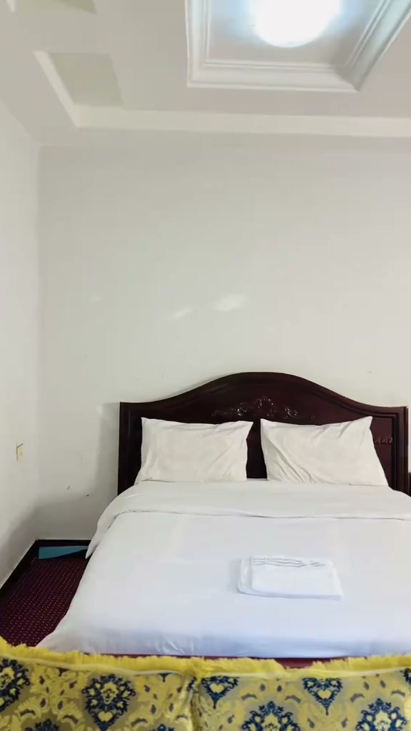 Direct frontal view of standard double bed with wooden headboard and ceiling detail at Gibe Hotel